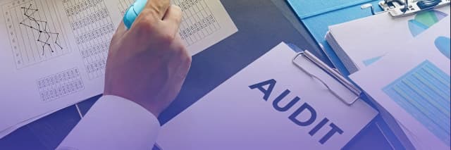 Close-up of a person reviewing audit documents with charts and a clipboard labeled “AUDIT,” symbolizing financial analysis and compliance.