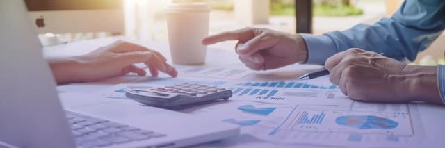 Two people reviewing financial charts and graphs on paper with a laptop and calculator on the table