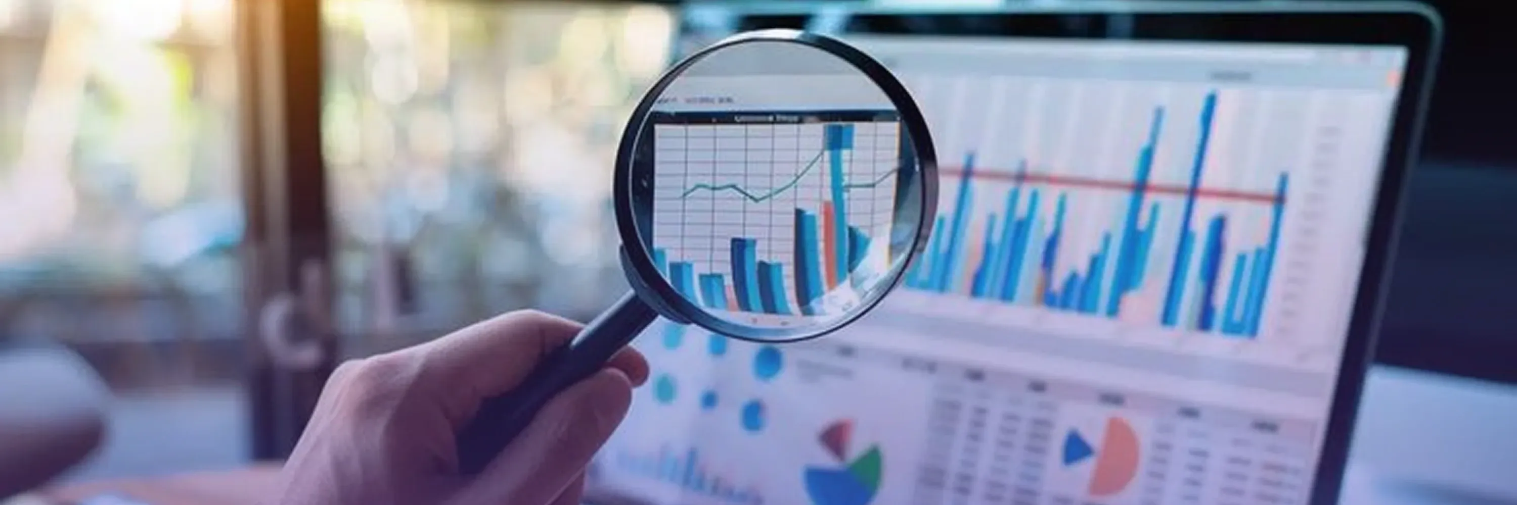 A magnifying glass highlights growth charts and financial data on a laptop screen, symbolizing detailed performance analysis and insights