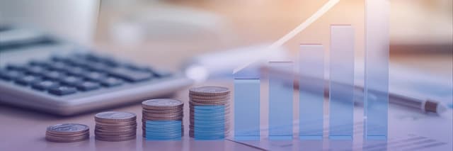 Stacked coins and rising bar charts on a desk with a calculator illustrate steady financial growth and positive business performance