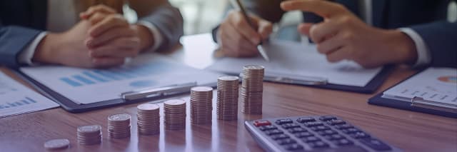 A close-up view of two professionals discussing financial reports with stacked coins and a calculator on the table