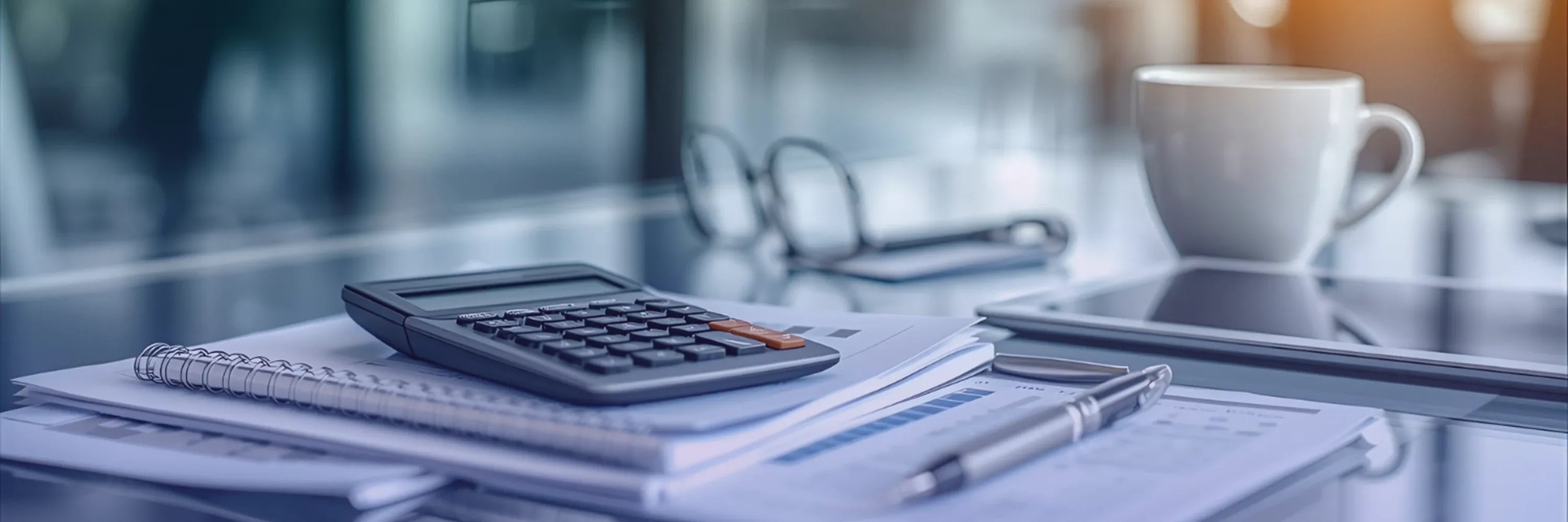 A close-up of an office desk with financial documents, a calculator, a pen, and a coffee cup in a modern, softly lit workspace