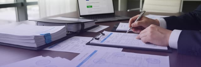 Business professional reviewing and signing official documents at desk with contract papers and laptop in office