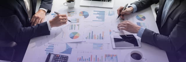 Business professionals analyzing financial reports and performance charts during a team meeting with documents, tablet, and calculator on the desk.