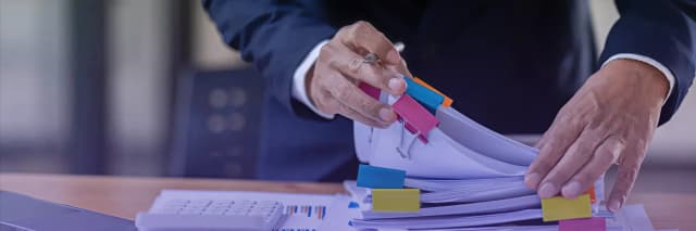 Business professional organizing and reviewing financial documents with color-coded tabs, highlighting structured document management and financial analysis workflow