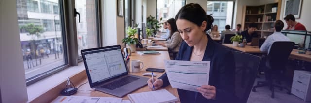 Business professional reviewing VAT tax return documents and financial reports on a laptop in an office environment