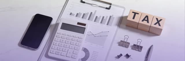 Flat lay image of business tax planning with a calculator, financial charts, smartphone, and wooden TAX blocks, illustrating financial analysis and accounting strategy