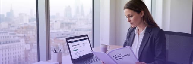 Businesswoman reviewing a VAT compliance guide while working on a laptop in a modern office