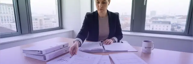 professional woman reviewing printed financial documents and organizing binders at office desk