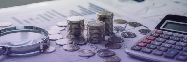 Stacks of coins, a calculator, and a magnifying glass on financial reports representing investment analysis, accounting, and financial planning