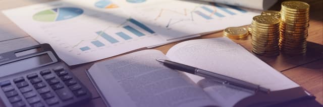 Financial analysis workspace with investment charts, stacked coins, calculator, and open notebook representing budgeting, accounting, and business planning.
