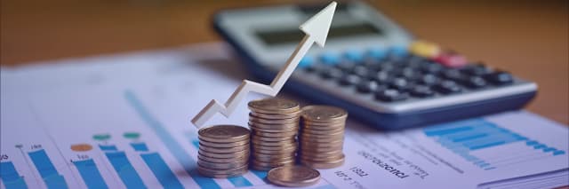 Stacks of coins with an upward arrow on a financial report next to a calculator represent investment growth, financial planning, and profitability analysis
