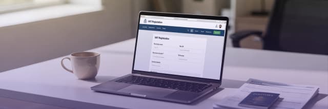 Laptop displaying an online VAT registration form with business documents and passport on a desk