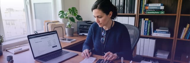 Small business owner managing finances with laptop, calculator, and receipts in a home office workspace