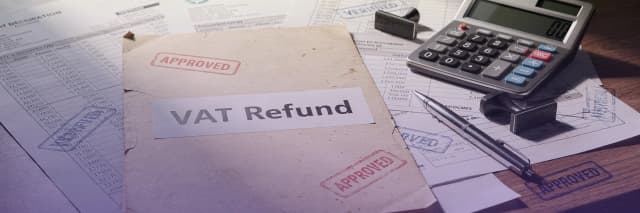 Approved VAT refund documents with invoices, stamps, calculator, and financial paperwork on a desk