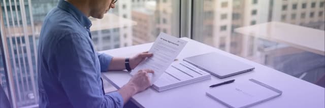Business professional reviewing a VAT registration guide and tax compliance documents at a modern office desk with laptop and paperwork