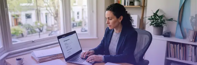 professional woman working on laptop completing VAT registration form at home office desk with documents and books