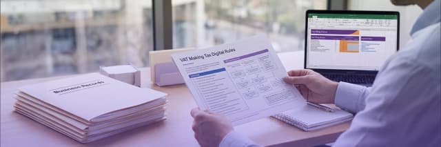 Business professional reviewing VAT Making Tax Digital compliance documents beside a laptop displaying tax filing spreadsheets and organized business records