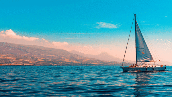 A charming sailboat drifting in the vast ocean, with soft waves lapping against its hull and a clear horizon ahead.