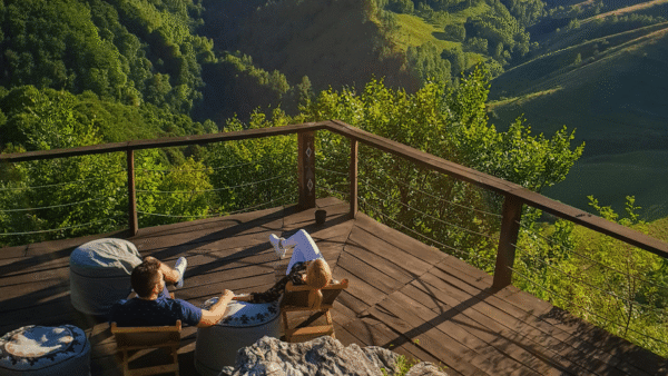 Two people relax on a deck, enjoying a stunning view of a lush valley in Romania